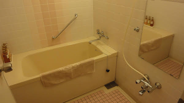 hotel suite bathing room with tiles on all walls and floor, a deep tub, and a faucet and mirror for washing